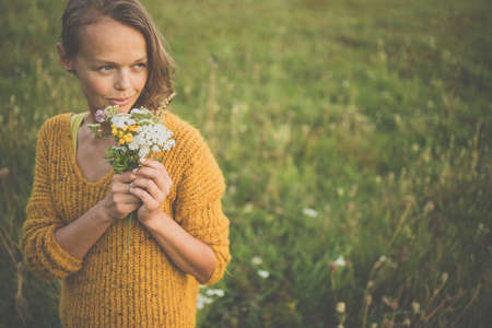 Beautiful young woman outdoors with a bouquet of wild flowers in a field, enjoying nature. Happy Woman on spring meadowの写真素材