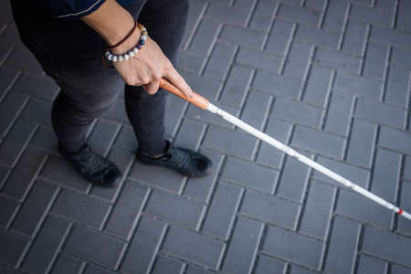 Blind woman walking on city streets, using her white cane to navigate the urban space better and to get to her destination safelyの写真素材