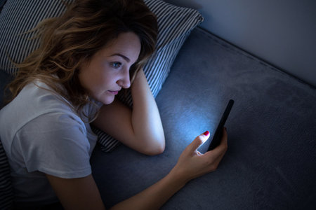 Young woman in bed holding a phone, tired and exhausted, blue light straining her eyes, messing up her circadian rhytmの写真素材