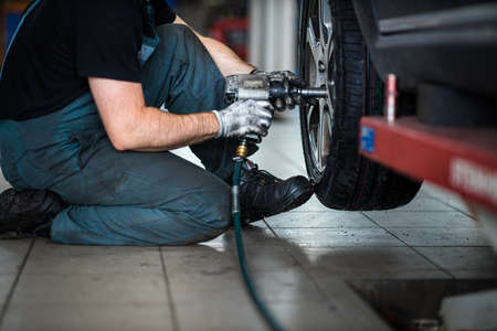 Car mechanic changing tires of a car in a repair shop,car garage (shallow DOF, colour toned image)の写真素材