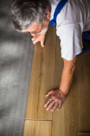 DIY, repair, building and home concept - close up of male hands lying parquet floor board/laminate flooring (shallow DOF; color toned image)の写真素材
