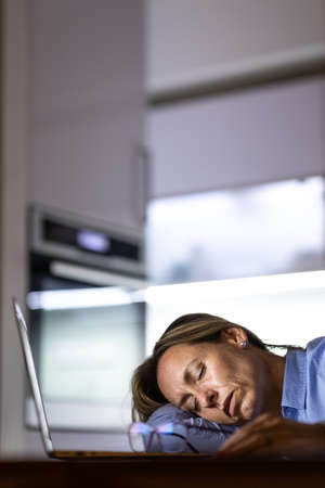 Pretty, middle-aged woman working late in the day on a laptop computer at home, running a business from home, working remotely - getting frustrated, exhaustedの写真素材