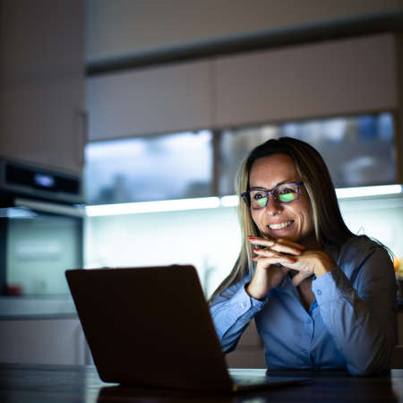 Pretty, middle-aged woman working late in the day on a laptop computer at home, running a business from home, working remotely - getting frustratedの写真素材