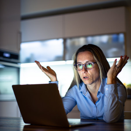 Pretty, middle-aged woman working late in the day on a laptop computer at home, running a business from home, working remotely - getting frustratedの写真素材