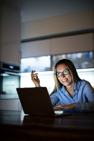 Pretty, middle-aged woman working late in the day on a laptop computer at home, running a business from home, working remotely - getting frustratedの写真素材