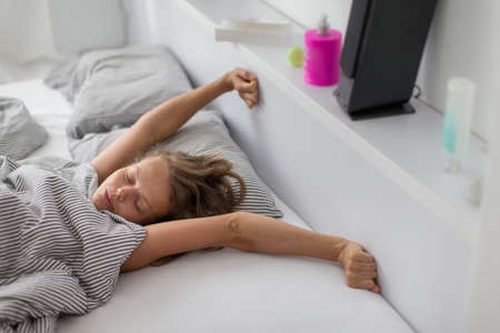 Pretty, young woman stretching in bed after waking upの写真素材