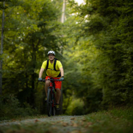 Young man with his mountain bike going for a ride past the city limits in a lovely forest, getting the daily cardio doseの写真素材