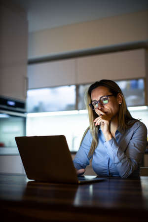 Pretty, middle-aged woman working late in the day on a laptop computer at home, running a business from home, working remotely - getting frustratedの写真素材