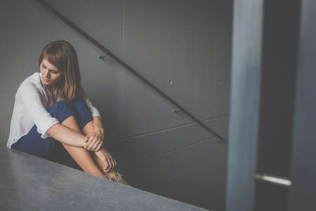 Depressed woman wearing medical face mask, looking out the window at an empty cityの写真素材