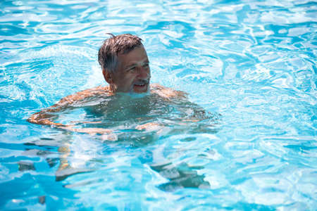 Senior man in his home swimming pool, enjoying the deserved retirementの写真素材