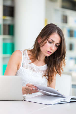 Pretty young college student in a library (shallow DOF; color toned image)の写真素材