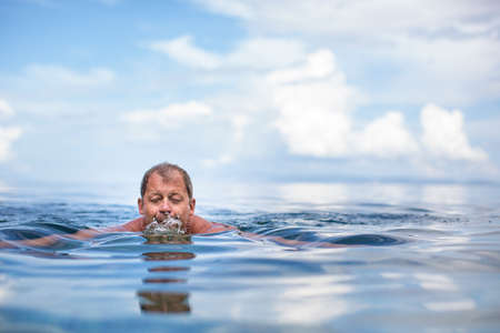 Senior man swimming in the Sea/Ocean - enjoying active retirement, having fun, taking care of himself, staying fitの写真素材