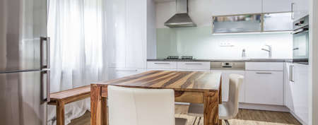 Modern Kitchen Interior Design Architecture Stock Image, Photo of a modern white kitchen with a dark wood table, hi-end appliances and plenty of daylightの写真素材