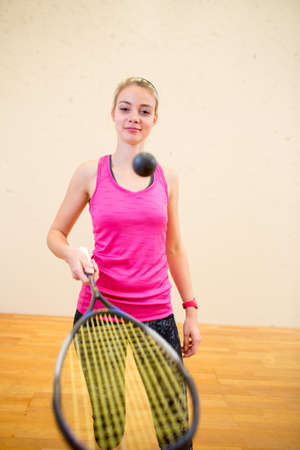 Cute young woman playing squash on a squash court, hitting the ballの写真素材
