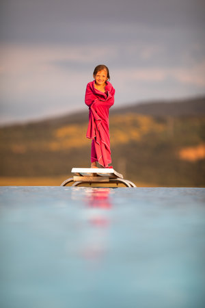 Little girl on a pool's edge, learning to swim and dive. Swimming with kids. Healthy sport activity for children. Sun protection. Water fun.の写真素材
