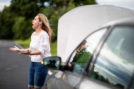 Pretty middle aged woman having car troubles - broken down car on the side of the road, calling the insurance company for assistanceの写真素材