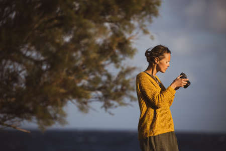 Pretty, young woman with a mirrorless camera, taking photos by the seaの写真素材