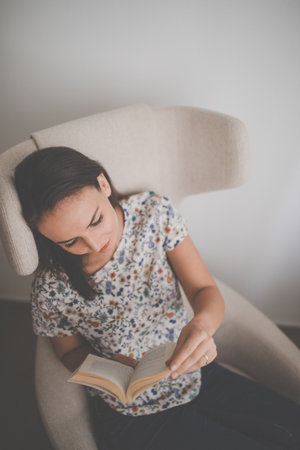 Cute young woman reading a book in a designer chair - color toned image, shallow DOFの写真素材