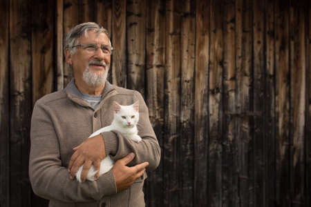 An elderly man holds a cute white kitten and smiles to the camera, selective focus, plenty of copy spaceの写真素材