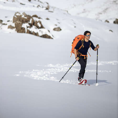 Winter sports - young man walking with snowshoes in high mountains covered with lots of snow (selective focus on the mountain in the background)の写真素材