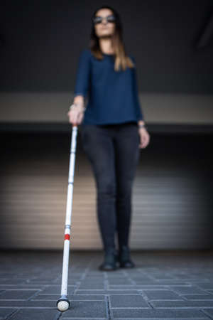 Blind woman walking on city streets, using her white cane to navigate the urban space better and to get to her destination safelyの写真素材