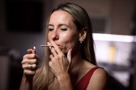 Mid-aged woman lighting a cigarette at home, getting her nicotine daily doseの写真素材