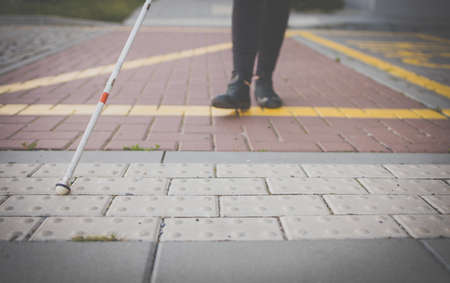 Blind woman walking on city streets, using her white cane to navigate the urban space better and to get to her destination safelyの写真素材