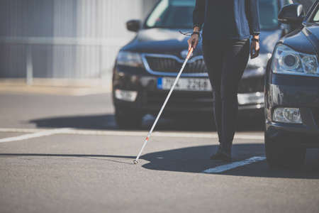 Blind woman walking on city streets, using her white cane to navigate the urban space better and to get to her destination safelyの写真素材