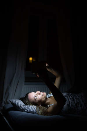 Middle-aged woman using her tablet computer before sleep in bed in the evening - exposure to blue light right before sleepの写真素材
