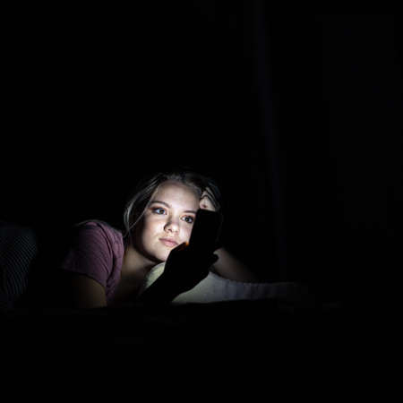 Teenage girl addicted to staying online and in touch with social networks checking her smart phone...