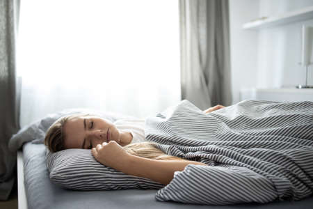 Pretty, young woman sleeping in her bed with her cell phone close to her. Smartphone in Bed Mobile / smartphone Addiction Concept.の写真素材