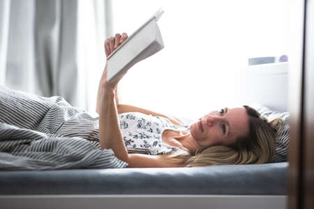 Pretty, middle-aged woman reading a book before sleep in bedの写真素材