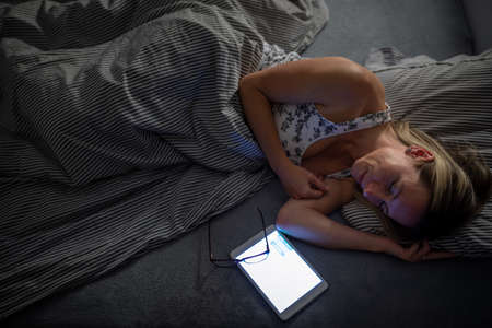 Middle-aged woman using her tablet computer before sleep in bed in the evening - exposure to blue light right before sleepの写真素材