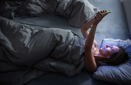 Middle-aged woman using her tablet computer before sleep in bed in the evening - exposure to blue light right before sleepの写真素材