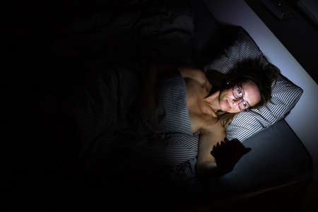Pretty, middle-aged woman using her cell phone in bed at night - unhealthy blue light exposureの写真素材