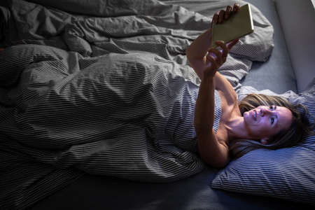 Middle-aged woman using her tablet computer before sleep in bed in the evening - exposure to blue light right before sleepの写真素材