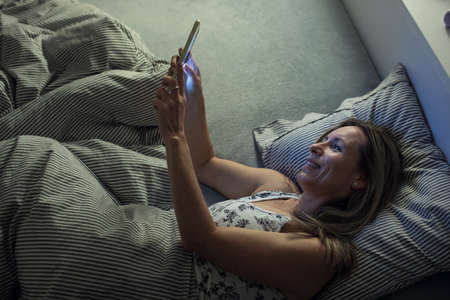 Pretty, middle-aged woman using her tablet computer before sleep in bed in the eveningの写真素材