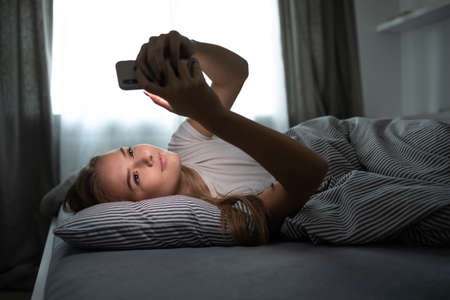 Pretty, young woman sleeping in her bed with her cell phone close to her. Smartphone in Bed Mobile / smartphone Addiction Concept.の写真素材