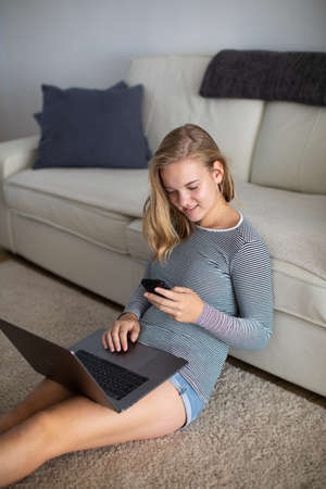 Teenage girl using her smart phone and laptop computer (shalllow DOF, color toned image)の写真素材