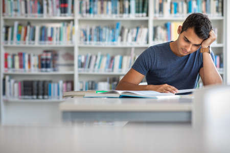Students in a library - handsome student reading a book for his class in a bright modern libraryの写真素材