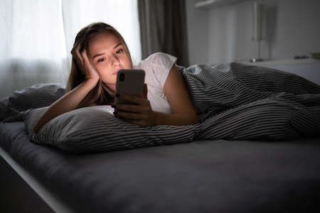 Pretty, young woman sleeping in her bed with her cell phone close to her. Smartphone in Bed Mobile / smartphone Addiction Concept.の写真素材