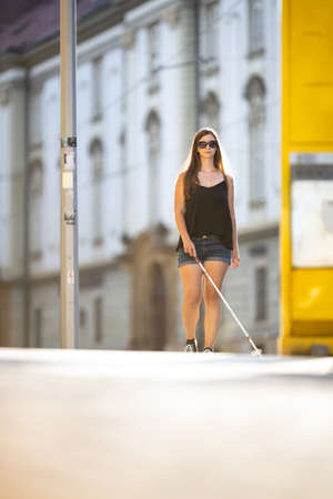 Blind woman walking on city streets, using her white cane to navigate the urban space better and to get to her destination safelyの写真素材