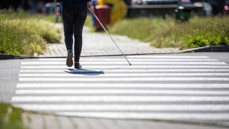 Blind woman walking on city streets, using her white cane to navigate the urban space better and to get to her destination safelyの写真素材