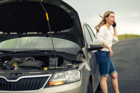 Pretty middle aged woman having car troubles - broken down car on the side of the road, calling the insurance company for assistanceの写真素材