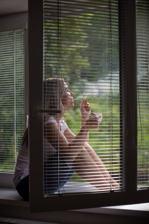 Mid-aged woman lighting a cigarette at home, getting her nicotine daily dose, unable to resist her unhealthy habitの写真素材