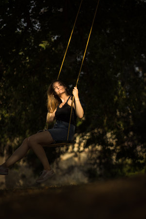 Carefree woman enjoying summer. Young woman is swinging on a swing in summer park garden.の写真素材