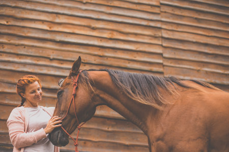 Pretty, young, redhead woman with her lovely horse, during her favorite leisureの写真素材