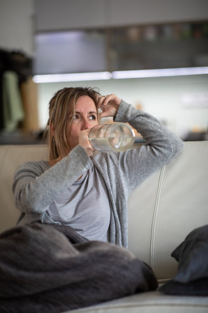 Midlle aged woman at home with a bottle of strong alcohol in her handsの写真素材