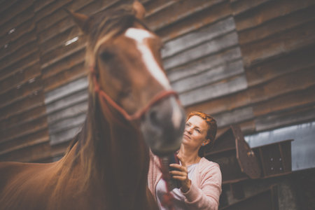 Pretty, young, redhead woman with her lovely horse, during her favorite leisureの写真素材