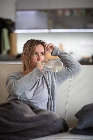 Midlle aged woman at home with a bottle of strong alcohol in her handsの写真素材